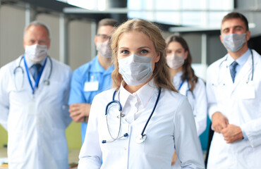 Fototapeta premium Female doctor in medical mask with group of happy successful colleagues also in preventive masks.