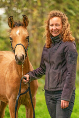 Obraz premium A light brown buckskin foal, the female owner stands next to the stallion Autumn Sun