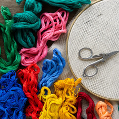 Flat lay of accessories for embroidery. Hoop, colorful floss threads, scissors and canvas, top view