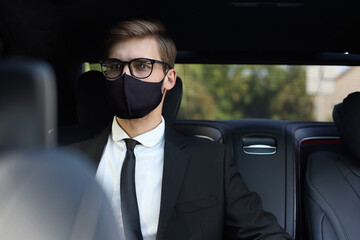 Thoughtful confident businessman in medical mask looking away while sitting in the car.