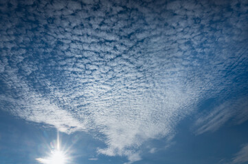 Schäfchenwolken und Sonne am blauen Himmel