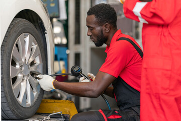 African mechanic working on maintenance the car in the garage ,using Tire-pressure gauge ,Garage and tires shop business concept