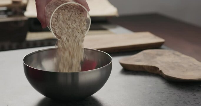 Slow motion making granola, pour oats in steel bowl on concrete countertop
