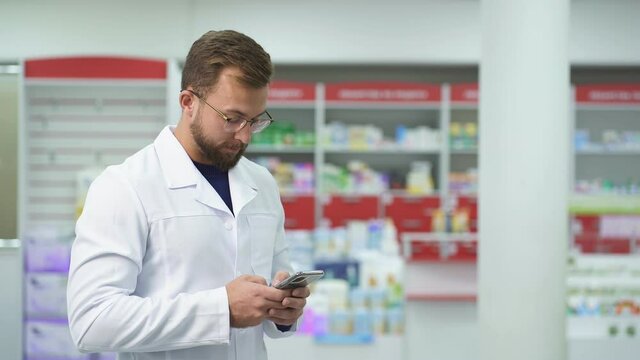 Portrait of beautiful man pharmacist in uniform at modern drugstore, attractive diligent druggist at work, ready to help customers