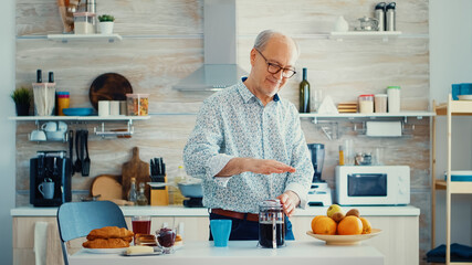 Happy senior man pushing on french press while preparing coffee for breakfast. Elderly person in...