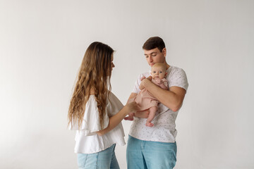 Young caucasian beautiful parents mom and dad hug and kiss their newborn daughter while standing on a white background
