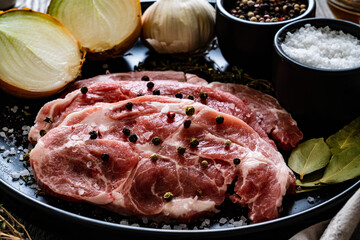 Raw pork chops with onion garlic and seasonings on plate on wooden table