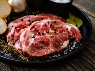 Raw pork chops with onion garlic and seasonings on plate on wooden table