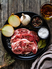 Raw pork chops with onion garlic and seasonings on plate on wooden table