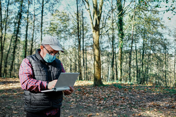 Fototapeta premium Mature man wearing mask working with laptop in field