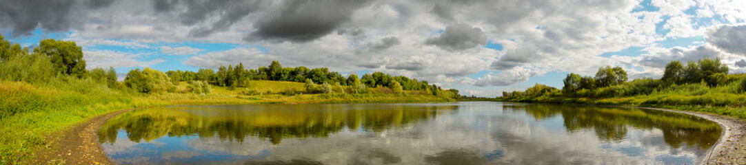 Summer panoramic landscape with calm river and beautiful clouds in blue sky