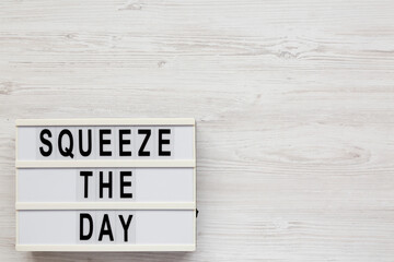 'Squeeze the day' on a lightbox on a white wooden background, overhead view. Flat lay, top view, from above. Copy space.