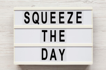 'Squeeze the day' on a lightbox on a white wooden surface, overhead view. Flat lay, top view, from above.