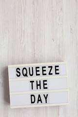 'Squeeze the day' on a lightbox on a white wooden background, overhead view. Flat lay, top view, from above. Copy space.