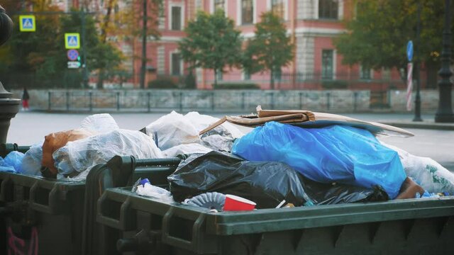 Trash spilling out of overfilled trash plastic bag on city street.