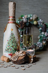 Champagne bottle, bottle cork, champagne glass, Christmas wreath, wooden figurine of an angel, candle on a wooden stand on a gray background.