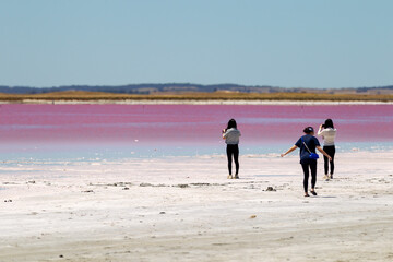 Fototapeta na wymiar Three tourists taking photos of the pink water at Meningie Pink Lake in South Australia on November 8th 2020