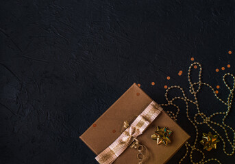 Gift box, gold sparkles, decorations on a black background. Christmas decor. Place for signature.