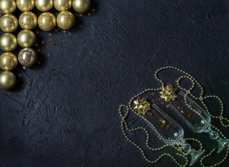 Champagne glasses with sparkles, gold glass balls, decorations on a black background. Christmas decor. Place for signature.