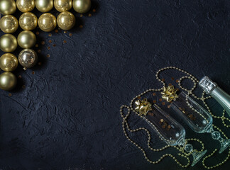 Champagne bottle, glitter wine glasses, gold glass balls, decorations on a black background. Christmas decor. Place for signature.