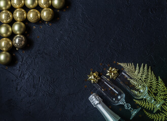 Obraz na płótnie Canvas Champagne bottle, sparkling wine glasses, golden glass balls, artificial branch, decorations on a black background.