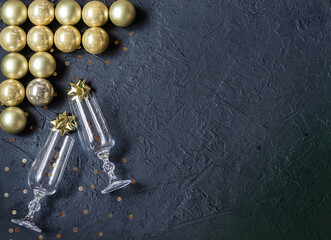 Glasses for wine with sparkles, gold glass balls, decorations on a black background. Christmas decor. Place for signature.
