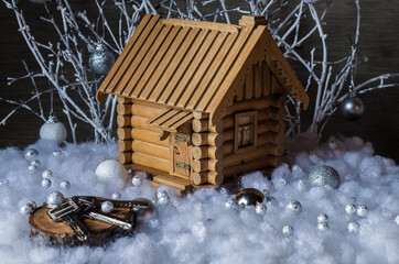 A mock-up of a wooden house with a cut of a tree and keys from the house in artificial snow against the background of white branches with glass balls. Christmas composition.