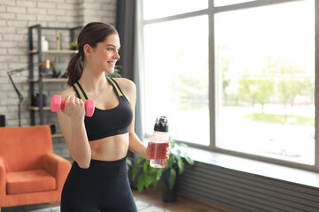 Fototapeta na wymiar Young beautiful woman standing with dumbbell and drink water after exercising. Attractive female bodybuilder working out. Fitness and healthy lifestyle concept.