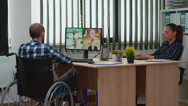 Paralysed, immobilized freelancer in wheelchair having videomeeting discussing online with coworkes in business office. Handicapped businessman working in financial company using modern technology.
