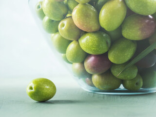 Freshly picked raw green olives in glass bowl on textured background.