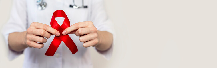 Red ribbon for aids and hiv world day support, close up. Hand of female doctor