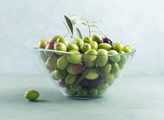Freshly picked raw green olives in glass bowl on textured background.