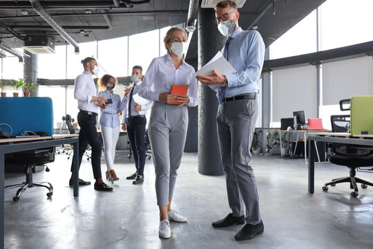 Group Of Modern Business People In Protective Masks Are Talking And Smiling While Standing In The Office Hallway