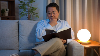 ソファーで本を読んでいる中年男性