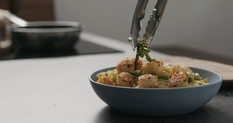 add asparagus to pesto fusilli with scallops in blue bowl on concrete countertop