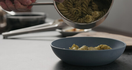 Slow motion pesto fusilli giganti fall into blue bowl on concrete countertop