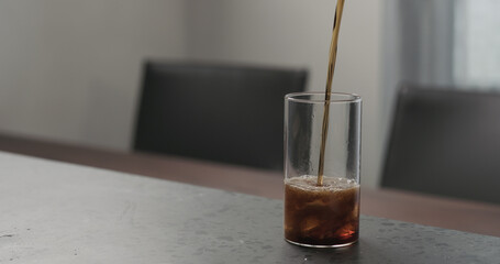 Slow motion pour cola into highball glass with crushed ice on concrete countertop with copy space