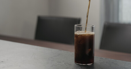 Slow motion pour cola into highball glass with crushed ice on concrete countertop with copy space