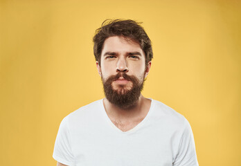 A man with a beard and mustache on a yellow background and a white T-shirt