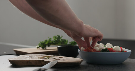 Slow motion man hands put mozzarella on top of kale in blue bowl on concrete surface