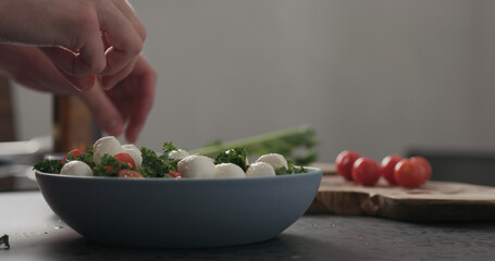 Slow motion man hands put mozzarella on top of kale in blue bowl on concrete surface