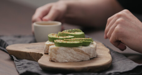 Slow motion man eating breakfast with caibatta with avocado and cream cheese and cup of espresso