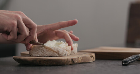 Slow motion man makes sandwich with cream cheese on olive board