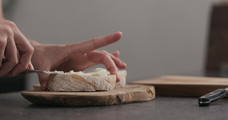 Slow motion man makes sandwich with cream cheese on olive board