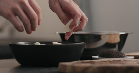 Slow motion man hands put mozzarella on top of kale in black bowl on concrete surface