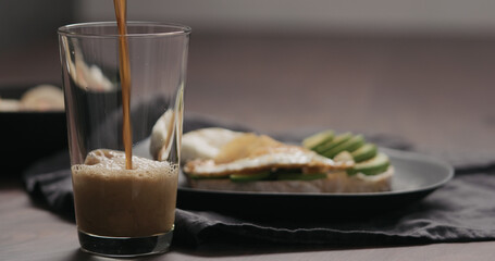 Slow motion pour stout beer into pint glass with food on background
