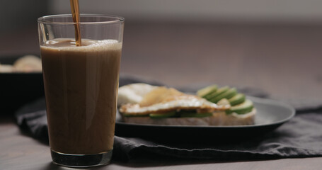 Slow motion pour stout beer into pint glass with food on background