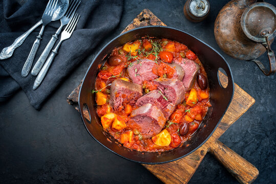 Modern Style traditionelle peruanische estofado de lengua gekochte Rinderzunge mit Gem&uuml;se und Oliven als Eintopf in einem Design Guss Topf