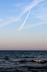 evocative image of sea at sunset with an airplane trail in the sky

