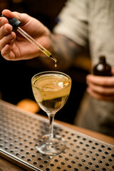 barman holds dropper with liquid and carefully adds it to glass with cocktail